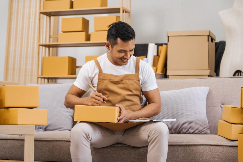 Men working from home, managing an online small business, sitting on the sofa, checking items, packing products, and preparing orders for shipment, ensuring timely delivery to customers