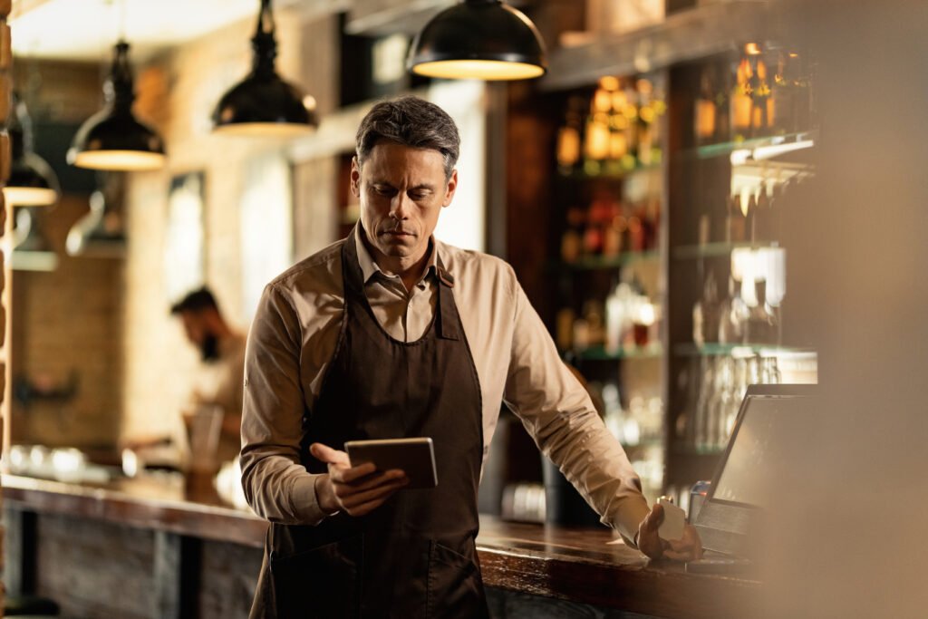 Mid adult barista using digital tablet at bar counter in a pub.