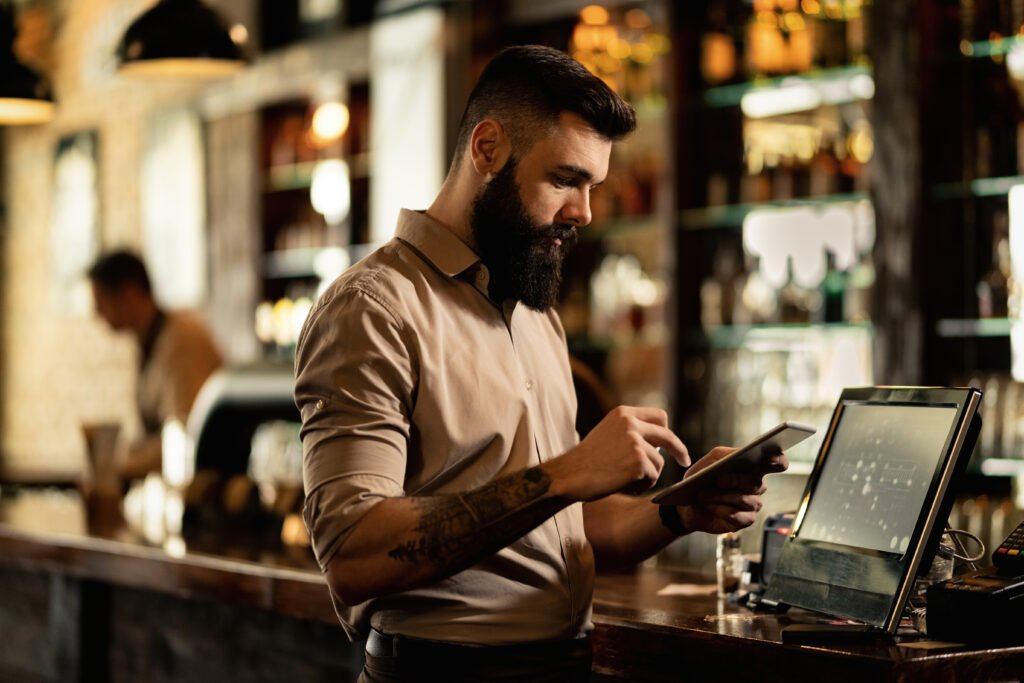 Young barista using touchpad while standing at cash register in a bar.