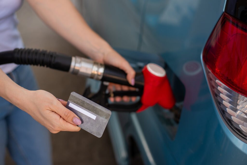 A woman fills her car with gasoline at a self-service gas station and holds a credit card