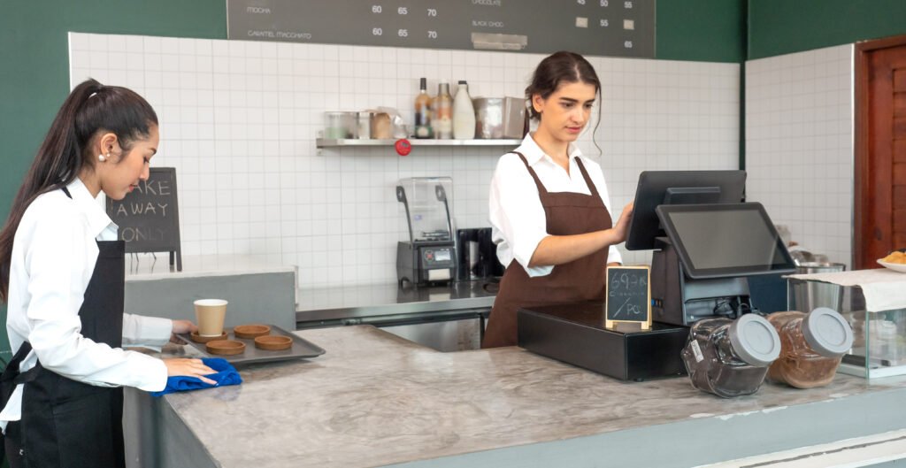 Beautiful female cashier standing at counter working with cash register in coffee shop retail service business. Small cafeteria business owner looking for sale transaction and checkout or payment.