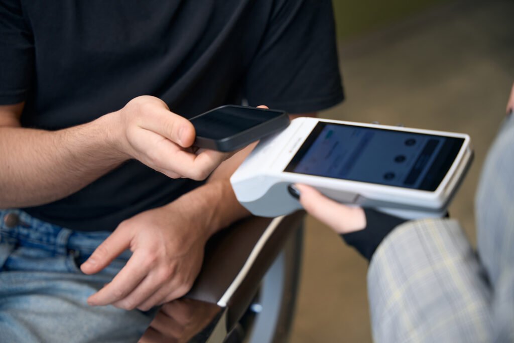 Unrecognizable customer paying in barbershop with smartphone and pos terminal