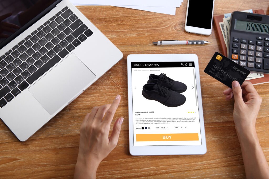 woman using credit card for buy black running shoes on ecommerce website via tablet with laptop, smartphone and office stationery on wooden desk